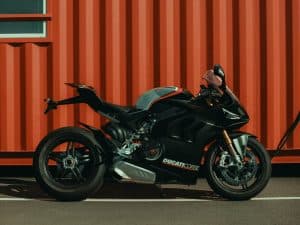 Black Ducati motorcycle parked in front of a shipping container, representing the process of preparing a motorcycle for secure international transport.